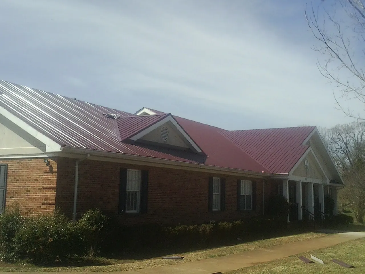 Red metal roof with gabled entries on a long brick building, from a Hail Damage Roof Repair job in Mahanoy City