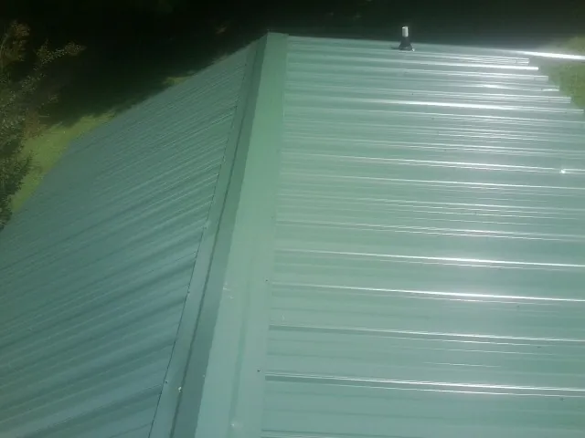 New green metal panels meeting at the ridge of a roof — Flat Roof Repair work by our crew in Mahanoy City