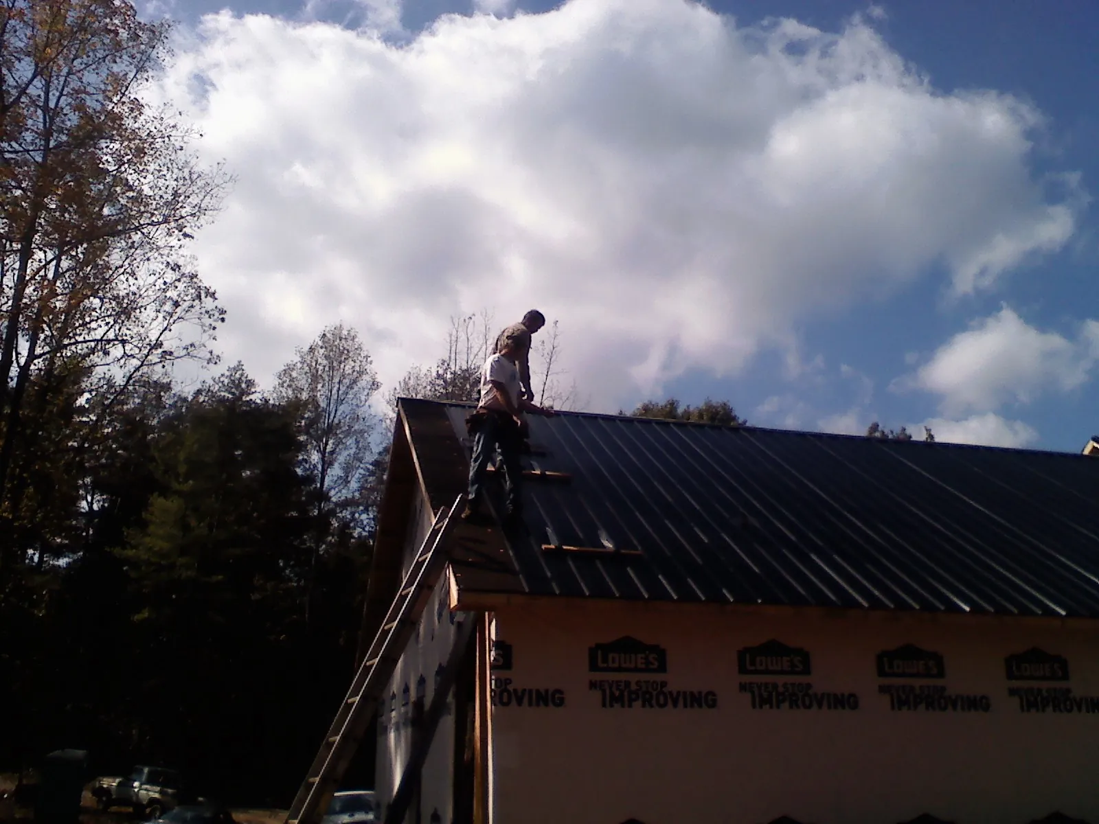 Roofer fastening dark metal panels high against a cloudy sky, from a Roof Inspection job in Mahanoy City