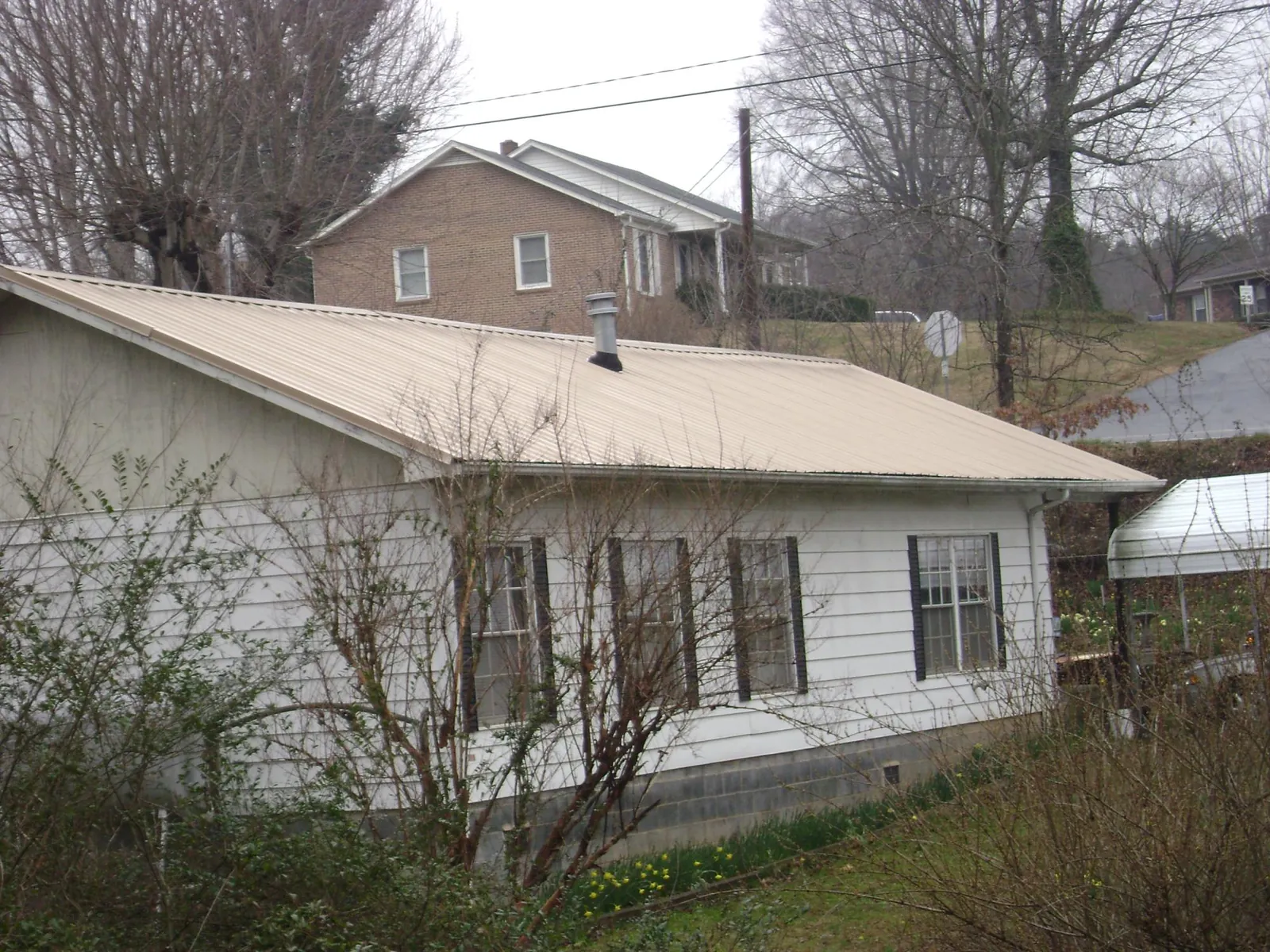 Tan metal roof on a white sided house set into a hillside — Commercial Roofing by Roofing Brothers in Mahanoy City